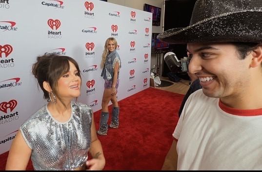 Ricky mid-interview with Maren Morris on the iHeartCountry Festival carpet, a microphone in frame.