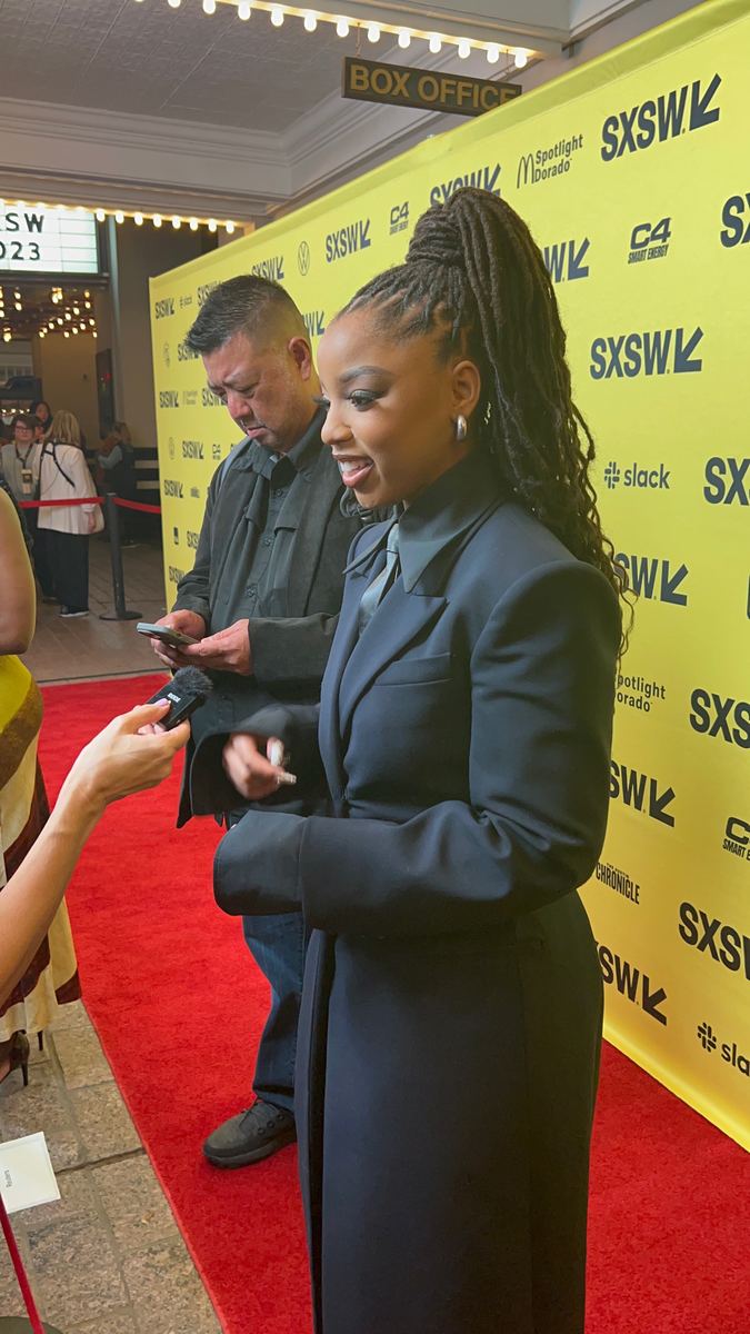 Chloe Bailey in a black suit on the SXSW carpet, speaking to someone holding a microphone.